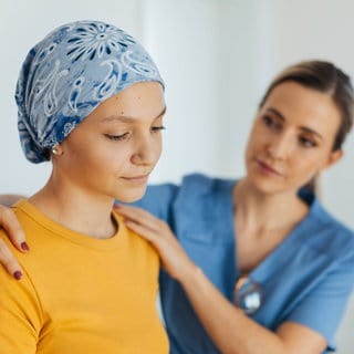 Junge Krebspatientin; Ärztin legt ihr aufmunternd die Hände auf die Schultern: Wer Krebs überlebt hat, leidet häufig jahrelang unter körperlichen und psychischen Folgen. Individuelle medizinische Angebote können die "Survivor" unterstützen. 