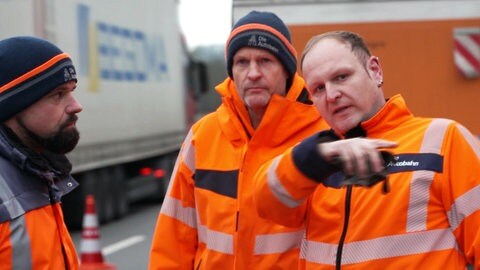 Drei Männer der Autobahnmeisterei stehen auf der Autobahn.