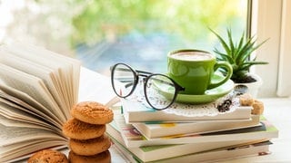verschiedene Bücher auf der Fensterbank mit einer Tasse Kaffee, Keksen und einer Blume