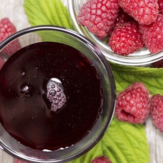 Frische Himbeeren und ein Glas mit Himbeersirup