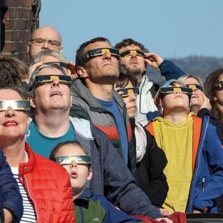 Symbolbild: Besucher mit Schutzbrillen blick in den Himmel