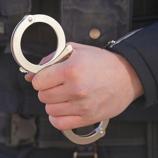 Ein Polizist hält Handschellen in der Hand (Symbolbild). Insgesamt drei Drogendealer sind von der Polizei in Ludwigshafen festgenommen worden. Die Polizei fand 27 Kilogramm Drogen.