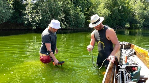 Jonas Hörrmann und Paul Schröter waten durch den hüfthohen Neckar in Tübingen. Mit einem Metallsuchgerät suchen sie nach einem Ehering, den Jonas beim Stocherkahnrennen verloren hat. 