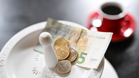 Geld liegt auf einem Teller vor einer Kaffeetasse | Aus der Sicht eines Kellners: Wie viel Trinkgeld ist angemessen?