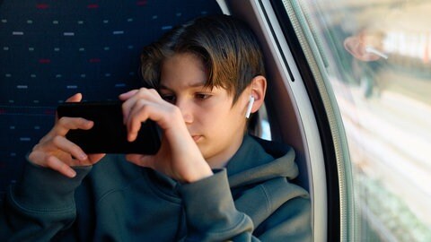 Ein Teenager mit Kopfhörern schaut auf sein Handy | Nutzen wir das Smartphone weniger, werden wir kreativer