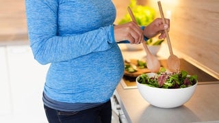 Eine Schwangere bereitet in der Küche einen Salat zu