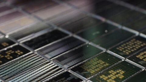 Nahaufnahme mehrerer photonischer Chips in rasterartiger Anordnung. Die Oberfläche der Chips zeigt komplexe Strukturen, die zur Verarbeitung von Licht und Photonen dienen. 