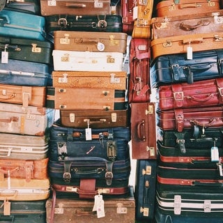 Viele verschiedene Koffer liegen aufeinander auf einem großen Stapel. Wie bekommen Sie Entschädigung und Schadensersatz bei verlorenem Gepäck, verspäteten Flügen, vorverlegten Flügen, Chaos am Flughafen, falschem Hotel und anderen Reisemängeln?