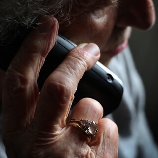 Eine ältere Frau mit einem Ring am Finger telefoniert. 