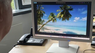 Ein Mann sitzt am Computer und sieht sich Urlaubsseiten an.