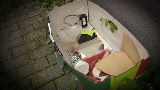 In einem Karton auf der Straße befinden sich verschiedene gebrauchte Kaffeeuntensilien. 