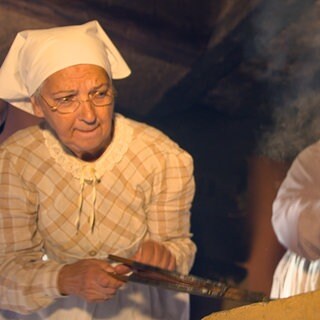 Zwei Frauen in historischen Klamotten kochen auf einem alten Herd.