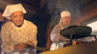 Zwei Frauen in historischen Klamotten kochen auf einem alten Herd.