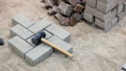 Hammer auf einem teilweise fertiggestellten Pflaster - Symbol für Handwerk beklagt steigende Kosten durch Staus auf der Rheinbrücke 