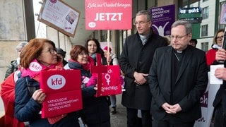 Bischof Georg Bätzing stehen vor der letzten Synodalversammlung mit Protestierenden zusammen.