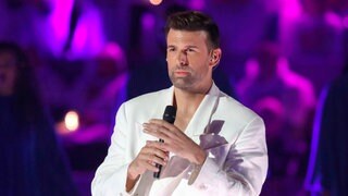 Sänger Jay Khan tritt in weißem Anzug mit Mikrofon auf der Bühne auf
