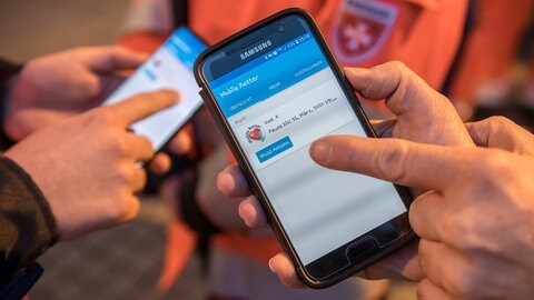 Zwei Rettungssanitäter bedienen die neue Ersthelfer-App Mobile Retter auf ihren Smartphones. Damit können sie nun auch außerhalb ihrer Dienstzeit per Smartphone-App alarmiert werden, um bei einem Herz-Kreislauf-Stillstand vor dem Eintreffen des Rettungsdienstes fachliche Hilfe leisten zu können.