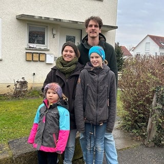 Eltern und zwei Töchter stehen vor dem Haus in dem sie wohnen.