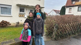 Eltern und zwei Töchter stehen vor dem Haus in dem sie wohnen.