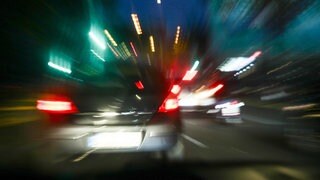 Das Symbolbild zeigt ein Auto, das nachts über eine Straße rast. 
