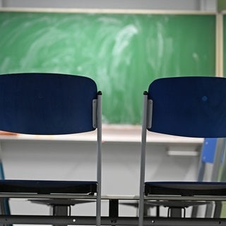 Zwei leere Stühle stehen in einem Klassenraum vor einer Tafel. Pisa-Studie: Deutsche Ergebnisse so schlecht wie nie.