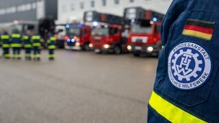 Am Logistikzentrum von dem Technischen Hilfswerk (THW) in Ulm stehen Mitarbeiter neben Einsatzfahrzeugen (Archivbild). 