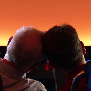 Ein Mann und eine Frau sitzen im Planetarium Stuttgart. Sie lehnen die Köpfe aneinander und schauen auf den Sternenhimmel.