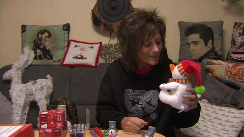 Ariane Weckbach sitzt auf einem Sofa und lächelt einen kleinen Schneemann aus Plüsch an, den sie in der Hand hält. Sie ist umgeben von Weihnachtsdekoration. 