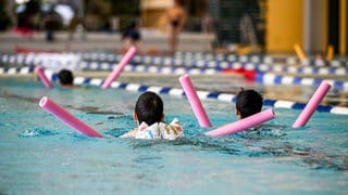 Kinder üben im Schwimmunterrticht im Hallenbad mit sogenannten Schwimmnudeln