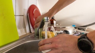 Ein Mann lässt Wasser aus dem Hahn an der Spüle in seiner Küche in ein Glas laufen.