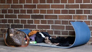 Verlassener Schlafplatz einer Obdachlosen. Eine Damenhandtasche, eine Isomatte und Kleidungsstücke liegen in einer Hofdurchfahrt.