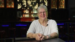 Seniorin sitzt an einer Theke und lächelt in die Kamera