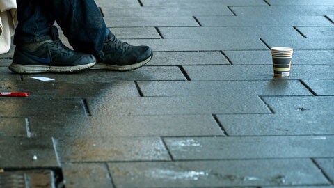 Füße eines Obdachlsoen, der einen Becher für Spenden aufgestellt hat. In Bad Kreuznach ist ein 13-Jähriger ermittelt worden, der einen Wohnsitzlosen mit einer Glasflasche angegriffen und verletzt haben soll