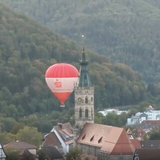 Ein Heißluftballon fährt in Bad Urach dicht an einem Kirchturm vorbei.