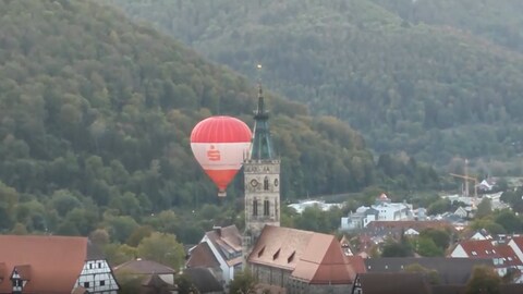 Ein Heißluftballon fährt in Bad Urach dicht an einem Kirchturm vorbei.