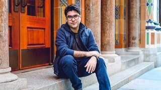 Der Theaterautor Nassim Soleimanpour auf einer Treppe sitzend.