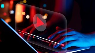 Zwei Hände tippen auf einem Laptop, der ein YouTube-Video anzeigt.