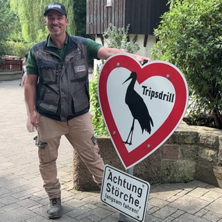 Ein Mann hält das wiederaufgetauchte Storchen-Schild von Tripsdrill in den Händen.