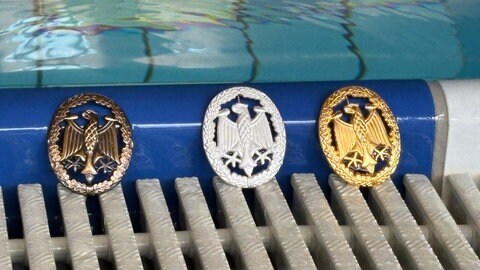 Drei Medaillen stehen am Rand eines Schwimmbeckens - in Ramstein haben Soldaten von US-Militär und Bundeswehr ein spezielles Sportabzeichen gemacht
