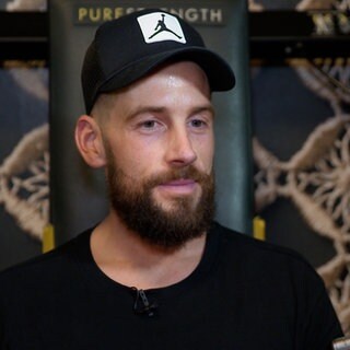Mann mit Kappe, Bart und schwarzem T-Shirt wird interviewt