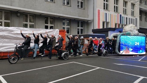 Studierende der Hochschule fahren auf einem Tandem mit 13 Sitzen, hintendran hängt der neue Fastnachtswagen.