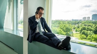 Dem Özdemir sitzt auf einer Fensterbank mit einem Smartphone und telefoniert. Der Grünen-Politiker setzt sich dafür ein, dass Soziale Netzwerke wie TikTok oder Instagram für Kinder und Jugendliche unter 16 Jahren verboten werden sollen.