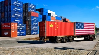 Container mit USA- und China-Fahne auf einem LKW, im Hintergrund gestapelte Container als Symbol für den Zollstreit zwischen USA und China