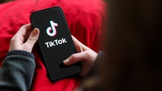 Ein Mädchen hält ein Smartphone, auf dem das TikTok-Logo zu sehen ist: Auf Social Media stoßen Kinder und Jugendliche schnell auf problematischen Content: Extremismus, Gewalt, Essstörungs-Communitys. Was braucht es für einen digitalen Jugendschutz?