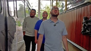 Die Straßenbahnfahrer Marco und Daniel Rungenhagen gehen mit einem Arbeitskollegen zwischen alten Straßenbahnen des Vereins Freunde der Freiburger Straßenbahn durch.