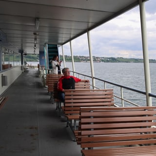 Pendlerin sitzt auf einer Bank auf der Bodenseefähre.