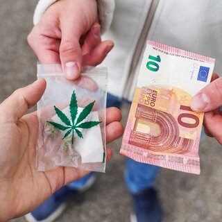 Zwei Männer tauschen eine Tüte mit Cannabis und einen Zehn-Euro-Schein.