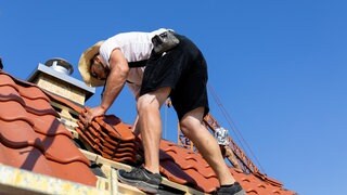 Dachdecker bei der Eindeckung eines Ziegeldaches. Die Temperaturen steigen an diesem Tag bis auf über 35 Grad