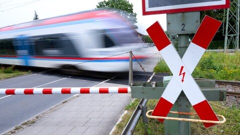 Ein Zug fährt an einer geschlossenen Bahnschranke vorbei (Symbolbild). Bei Wittighausen ist ein Regionalexpress in einen gefällten Baum gekracht. 200 Reisende saßen im Zug fest. Er wurde evakuiert.