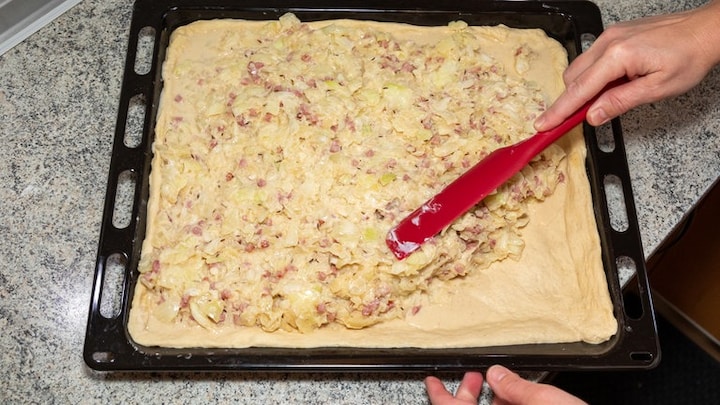Gemäß Rezept wird die Zwiebelmasse auf dem ausgerollten Hefeteig auf dem Blech verteilt.